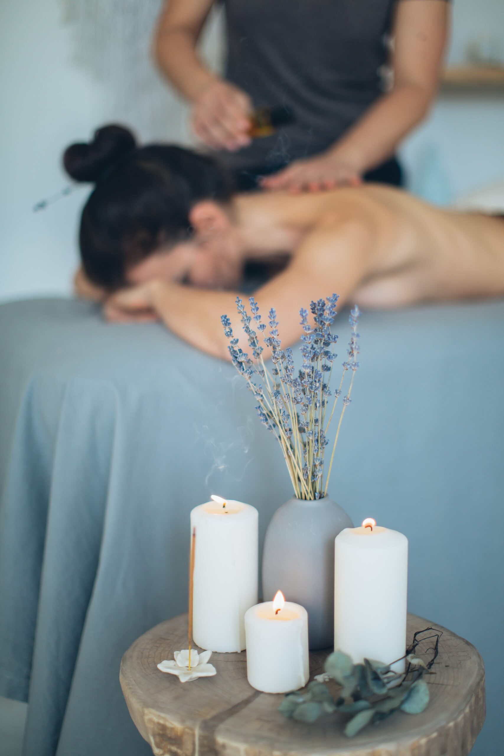 Mujer acostada recibiendo un masaje en la espalda junto a una mesa de velas con aromaterapia